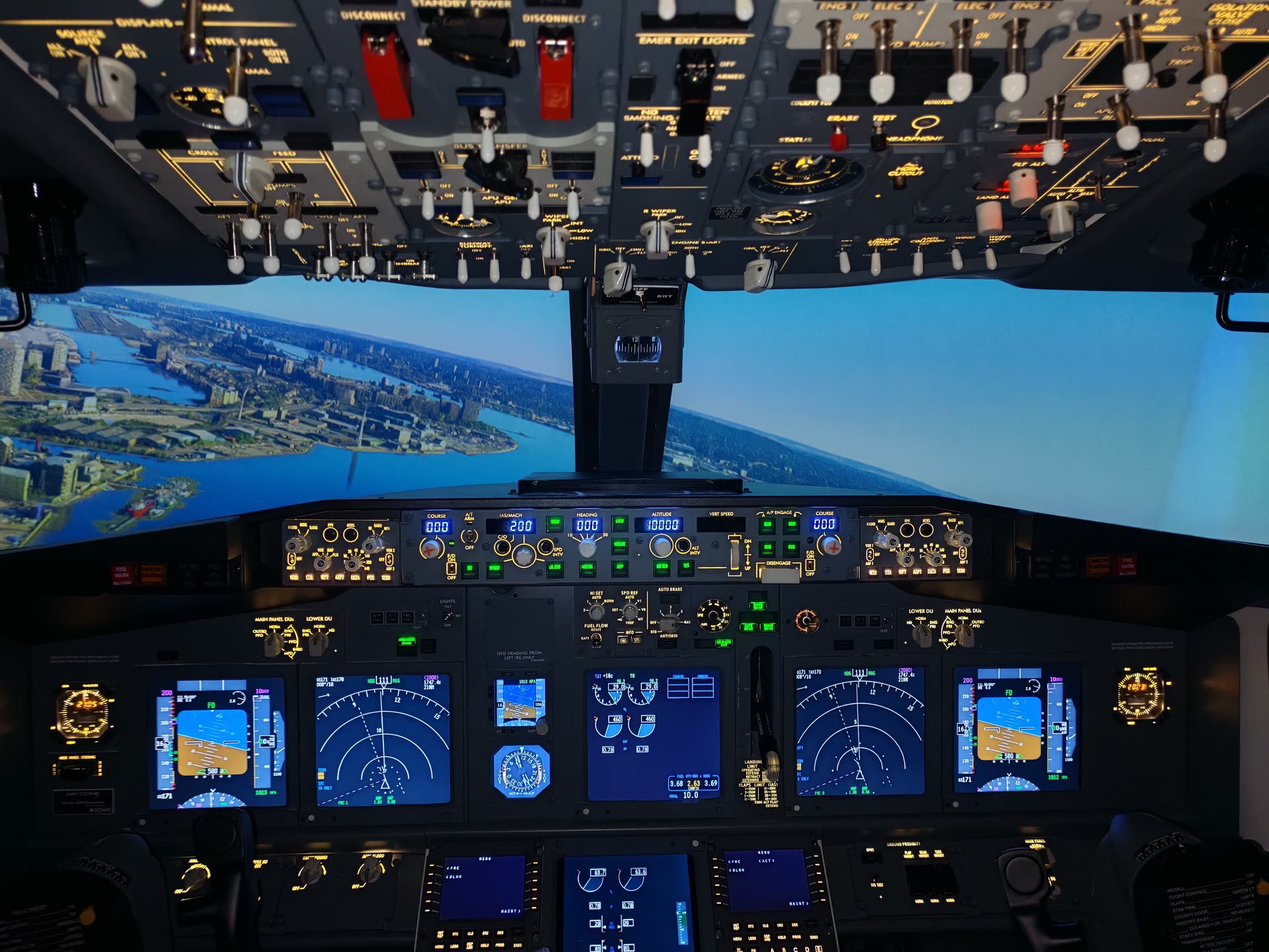Empty cockpit above a city, twin control columns and six glowing displays, with streets visible far below
