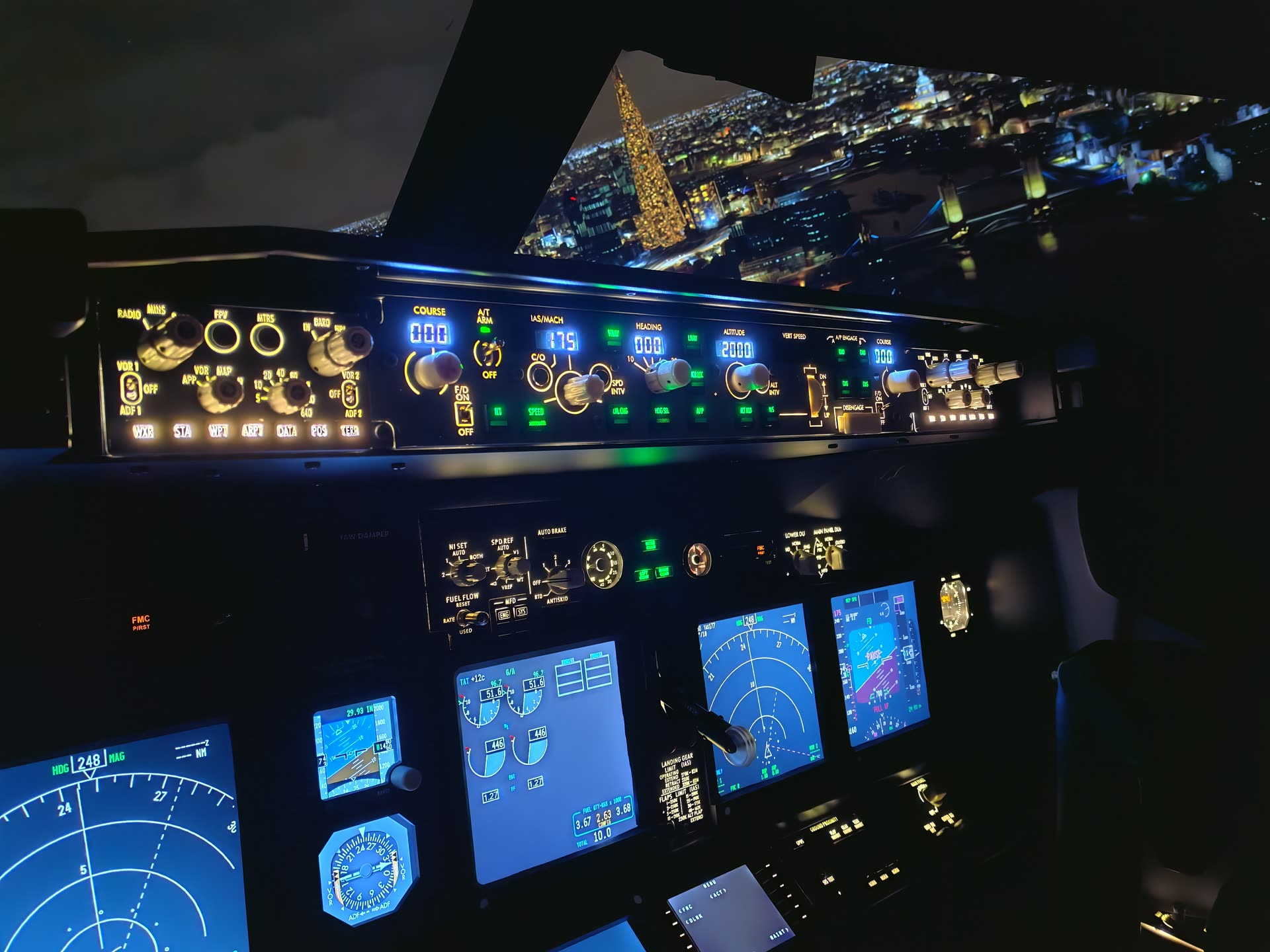 MCP glare shield lit at night, city lights blazing through the curved windshield from altitude