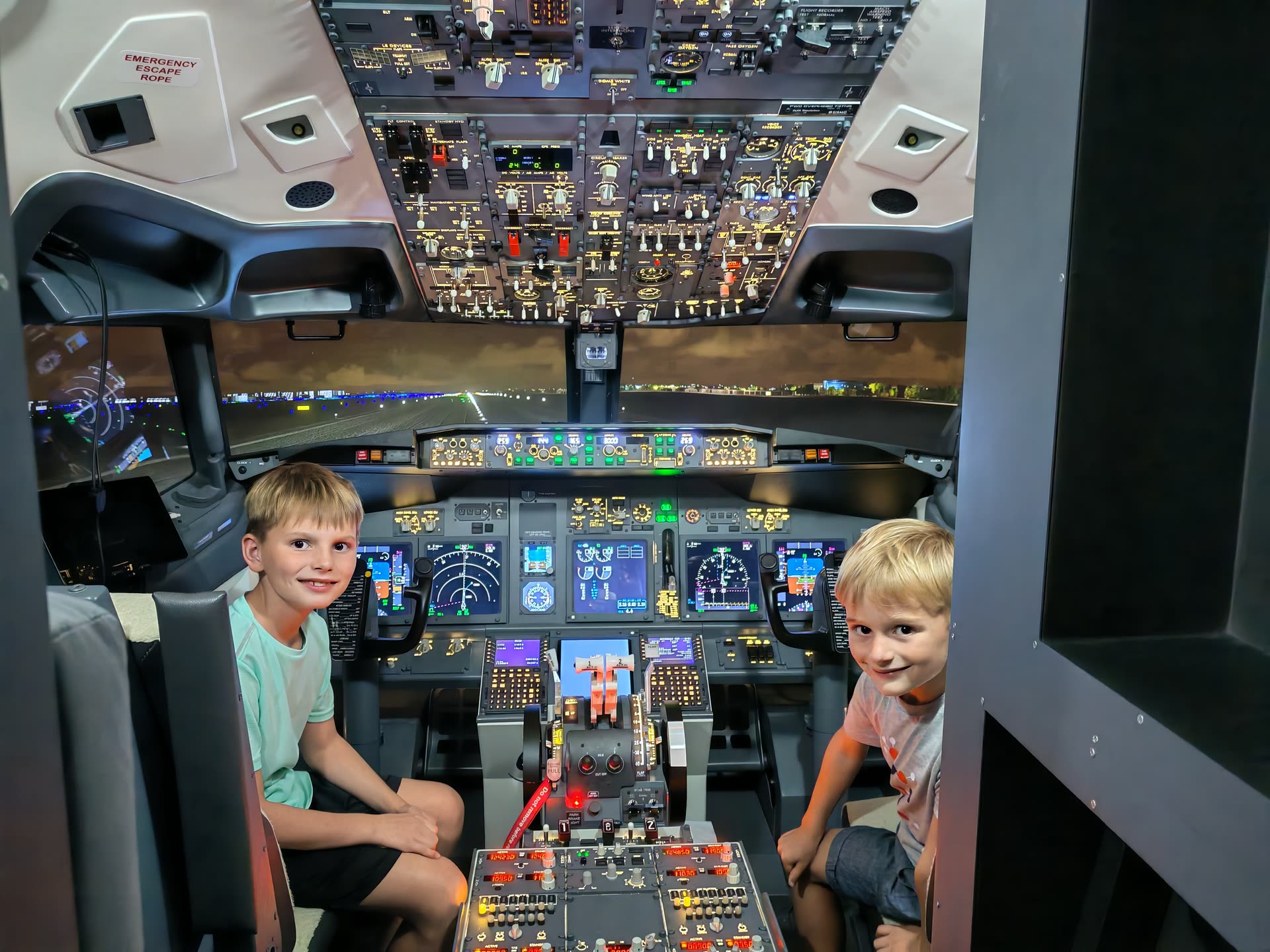 Two young brothers grinning in the pilot seats, the full 737 flight deck spread out behind them