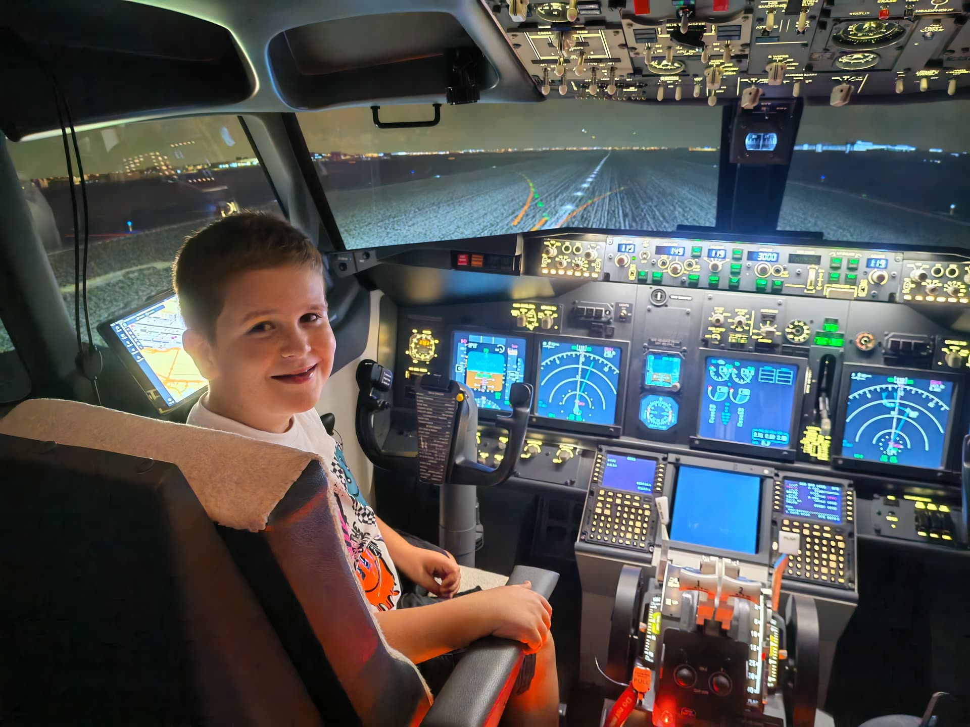 Young guest alone at the controls, runway lights stretching ahead on a night departure